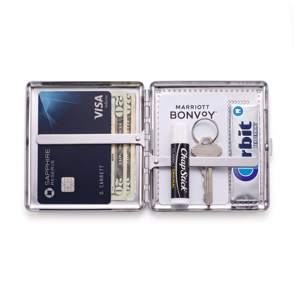 Chrome cardholder wallet open, holding a metal card, cash, a hotel key card, lip balm, a key and gum